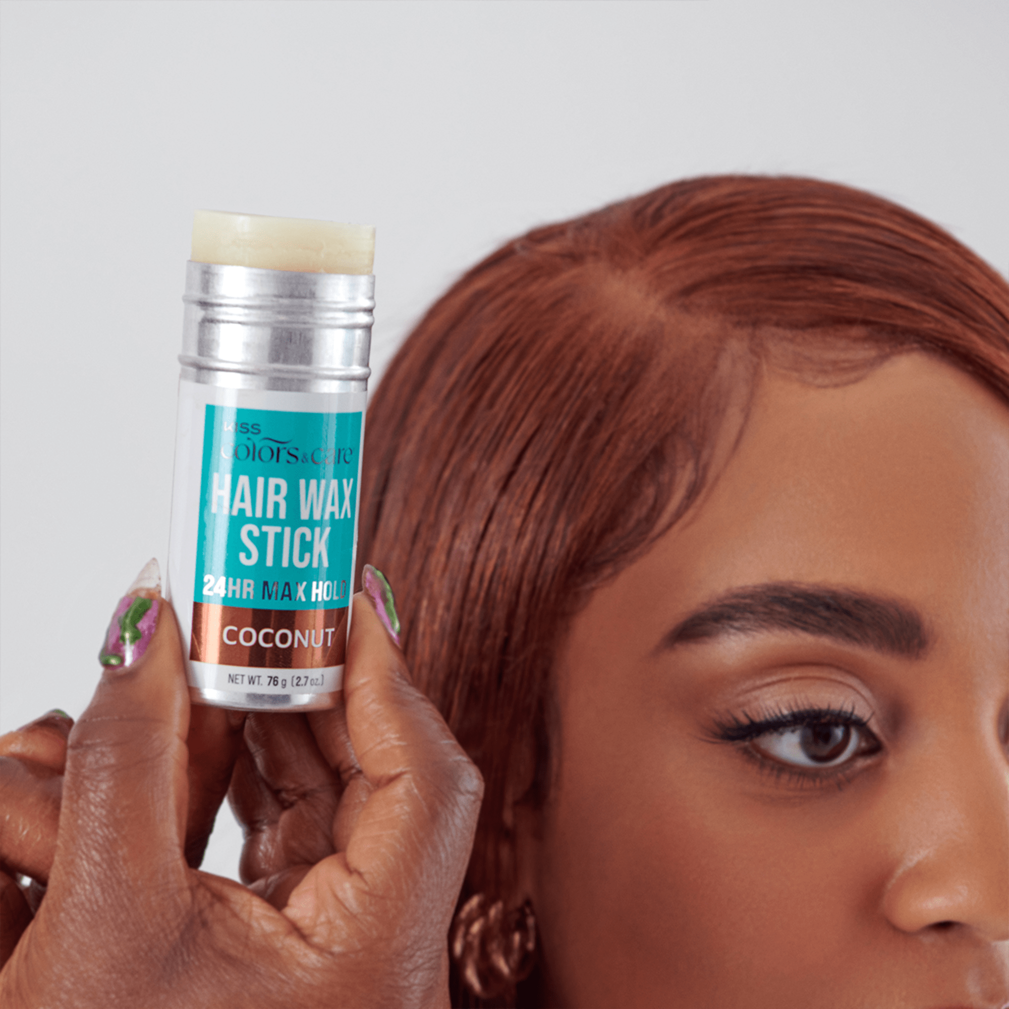 Hand holding a silver and turquoise KISS Colors &amp; Care Hair Wax Stick labeled "24HR Max Hold Coconut," next to a woman with styled red hair edges.