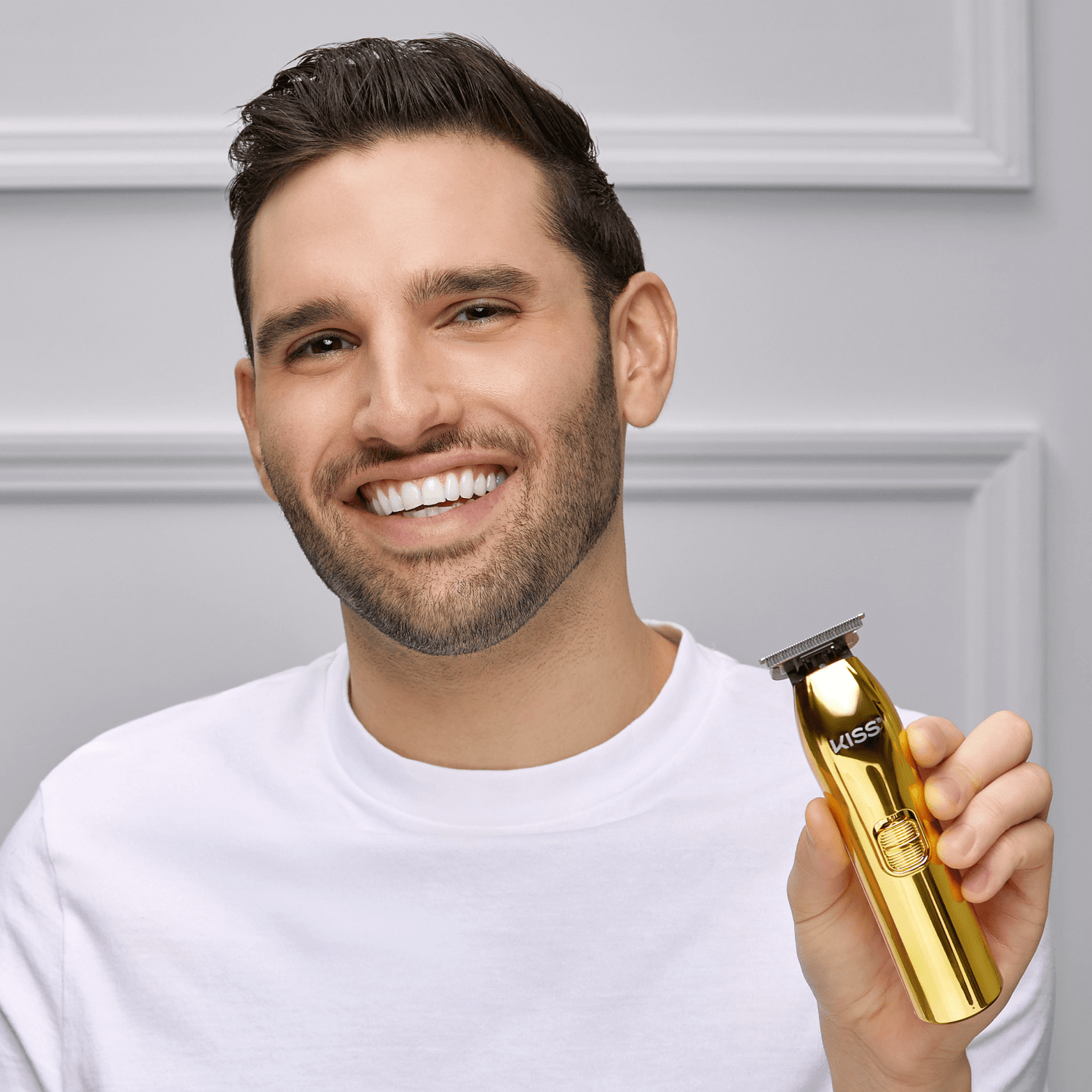 Smiling man in a white shirt holding a shiny gold cordless T-blade trimmer labeled \
