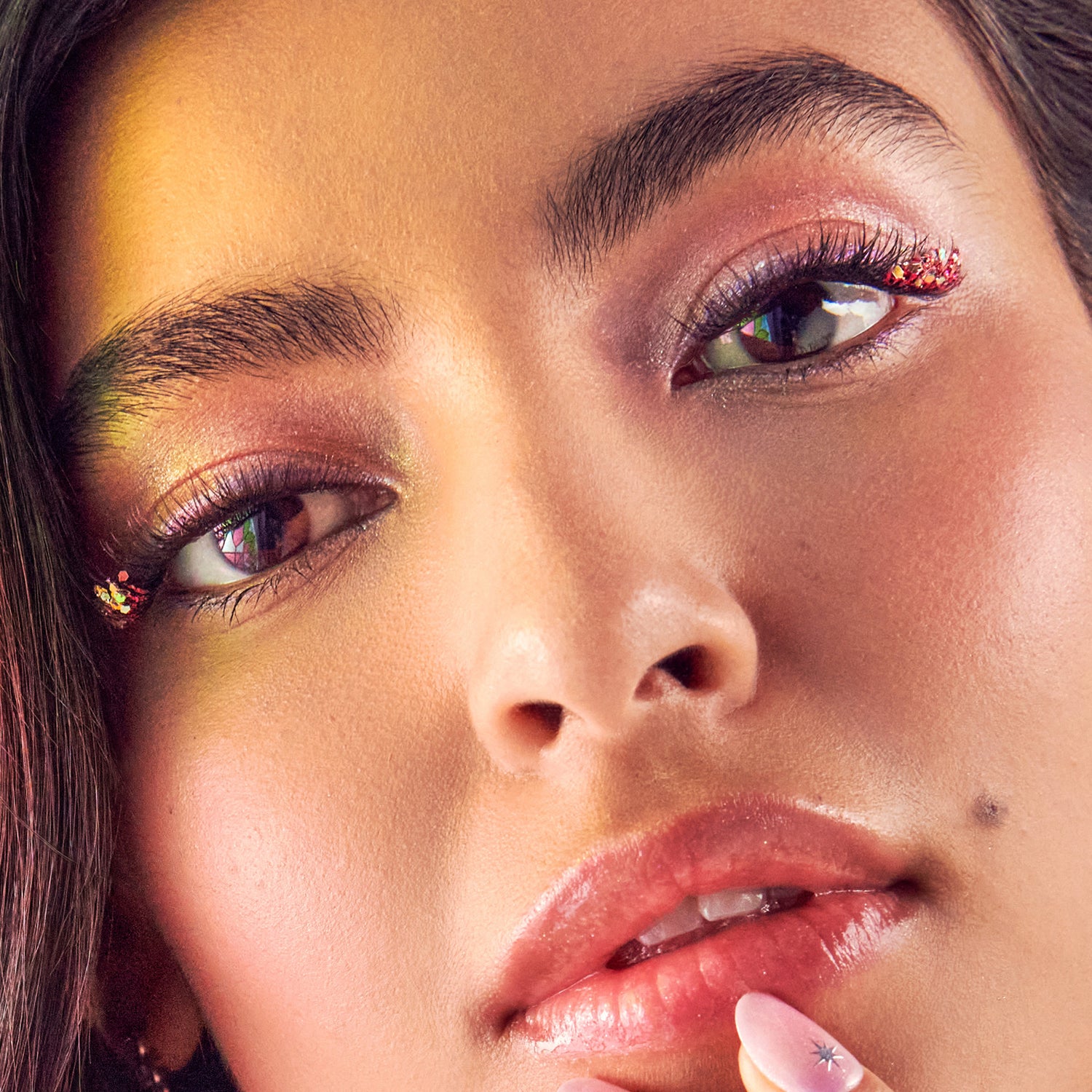 Woman with colorful eyeshadow in gold and burgundy, glittery eye makeup, and red glossy lips.
