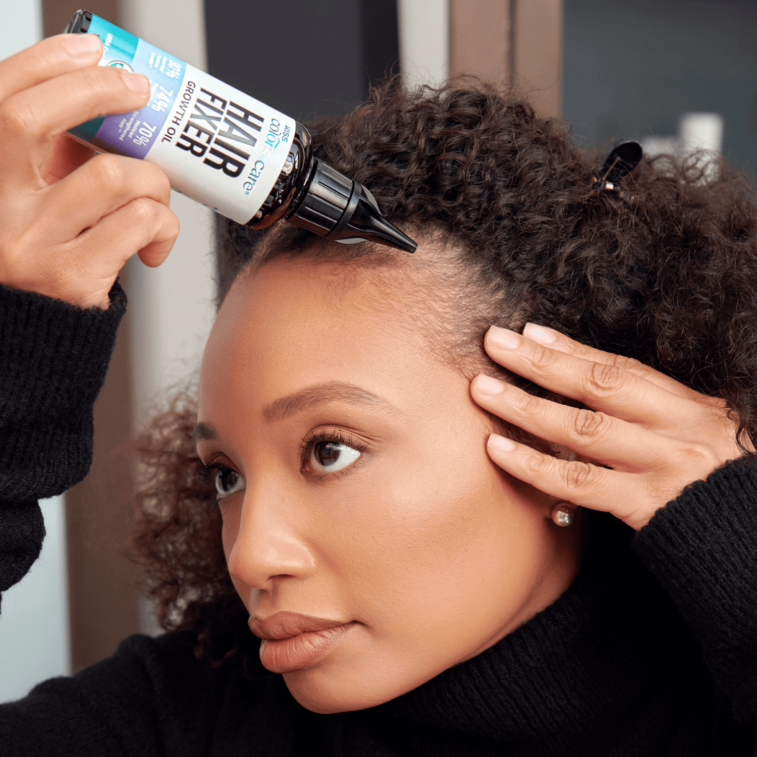 Woman with curly hair applies Hair Fixer Growth Oil from a small brown bottle labeled “Hair Fixer Growth Oil” by Kiss Colors and Care.