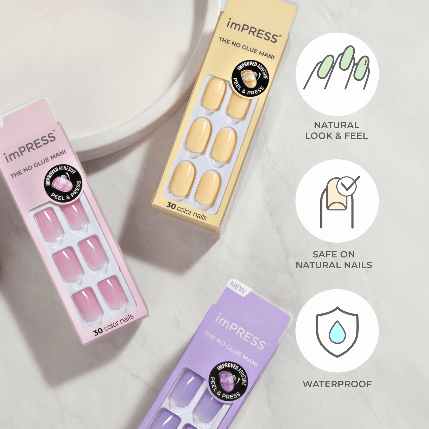Three packages of imPRESS press-on nails in pastel pink, yellow, and lavender hues on a marble surface. Each package contains 30 color nails and highlights \