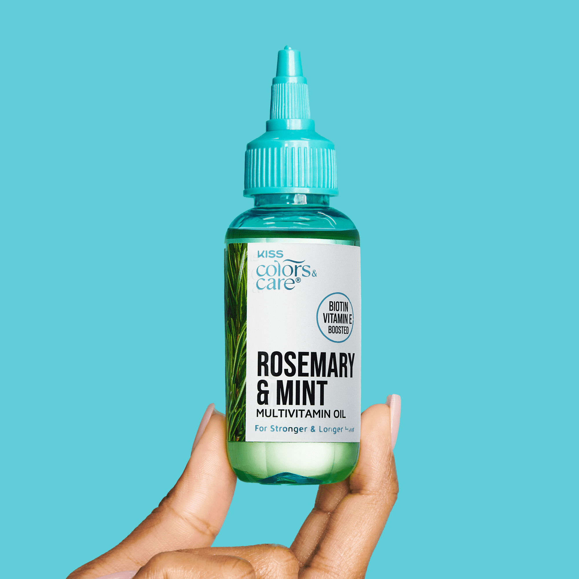 Hand holding a small clear green bottle with turquoise cap labeled "Rosemary &amp; Mint Multivitamin Oil" from KISS Colors &amp; Care, for stronger and longer hair.