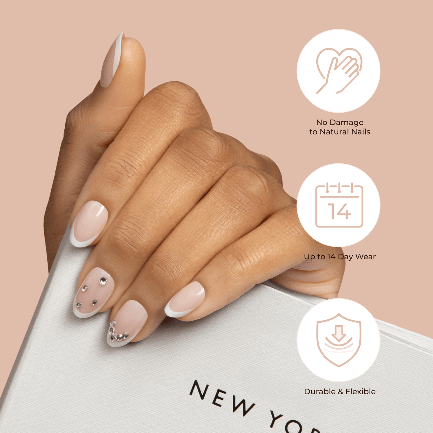Hand with nude press-on nails featuring white French tips and small rhinestones, holding a white book; icons highlight no damage, 14-day wear, and durability.