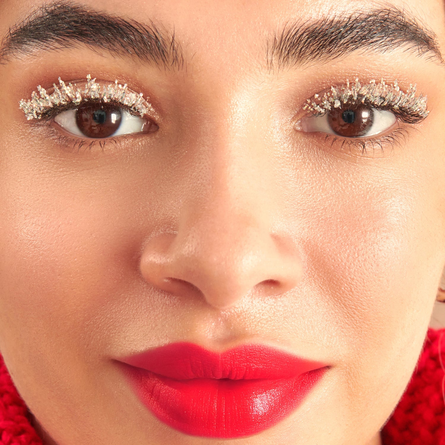 Close-up of makeup look featuring glittery eyeshadow, bold red lips, and defined brows.