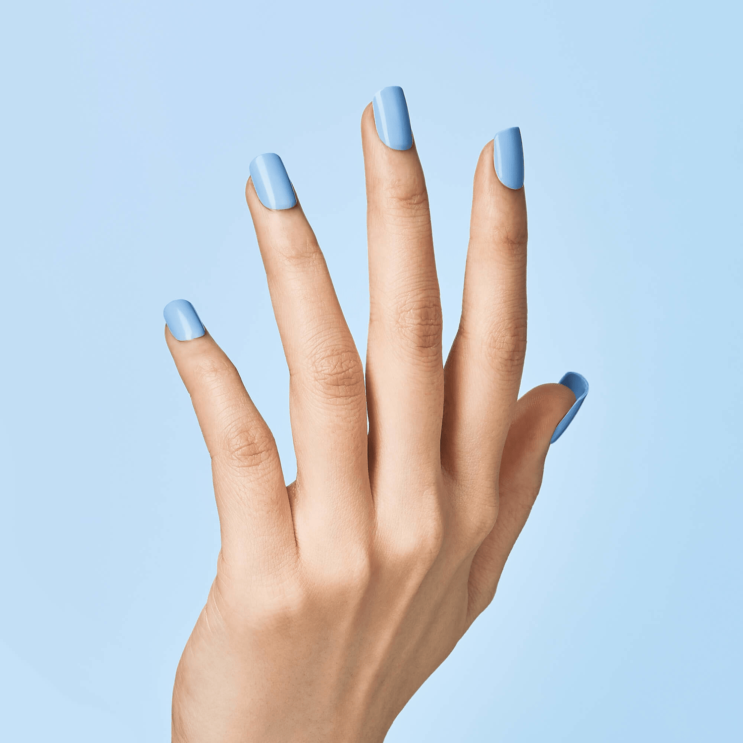 Hand with light skin tone displaying press on nails in solid baby blue color against a matching light blue background.
