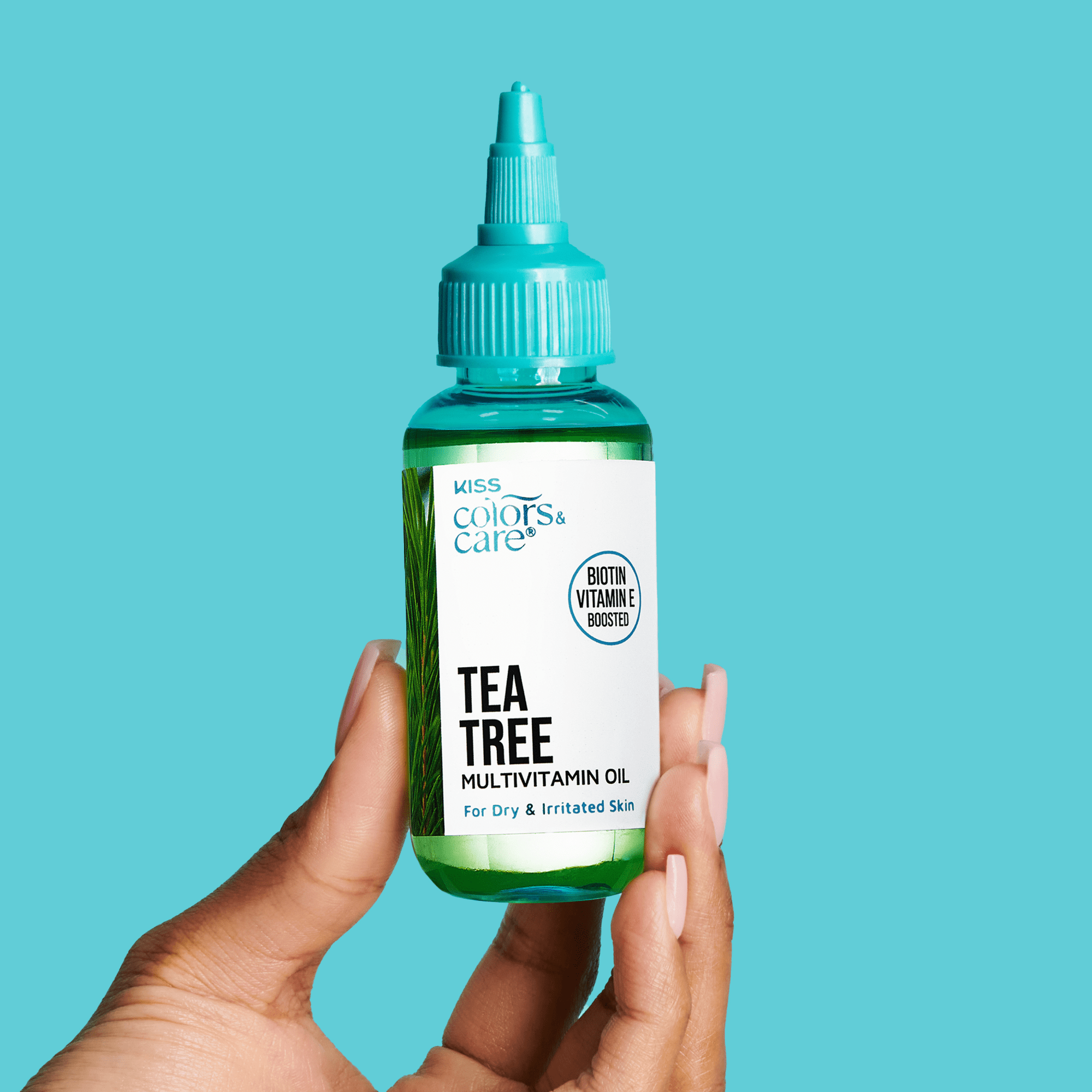 Hand holding a small green bottle of KISS Colors &amp; Care Tea Tree Multivitamin Oil with a blue dropper cap, labeled for dry and irritated skin, biotin and vitamin E boosted.