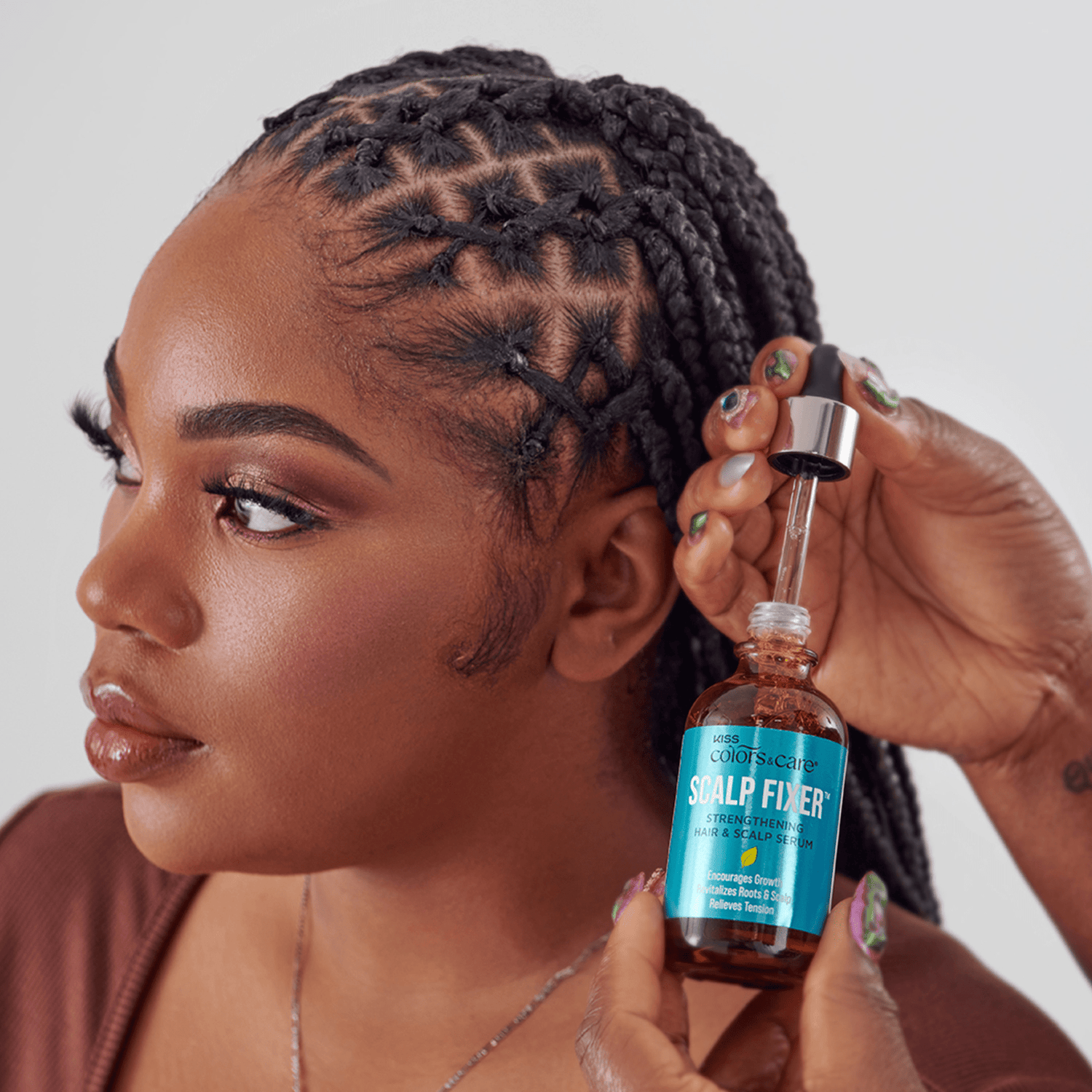 Woman with styled braided hair holding a bottle of KISS Colors &amp; Care Scalp Fixer serum with dropper, labeled for strengthening hair and scalp.