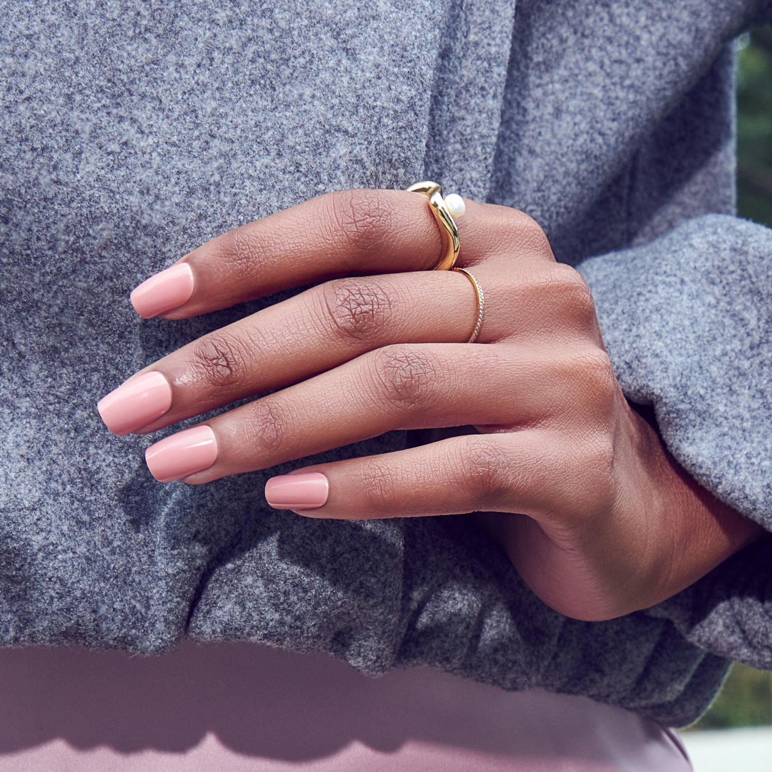 Hand with pink nails wearing gold rings against gray sweater