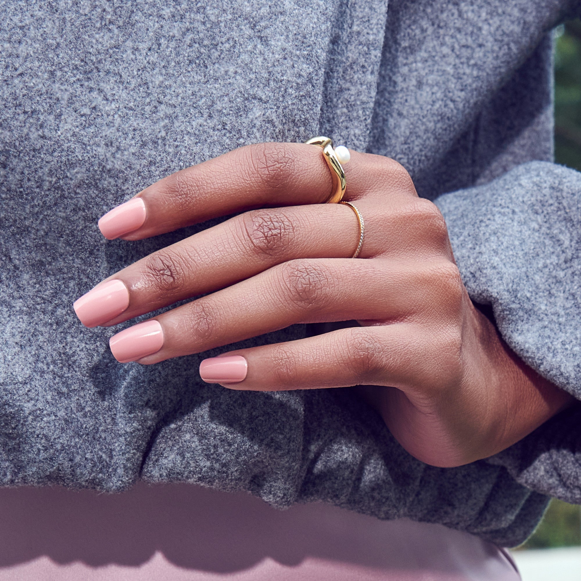 Hand with pink nails wearing gold rings against gray sweater
