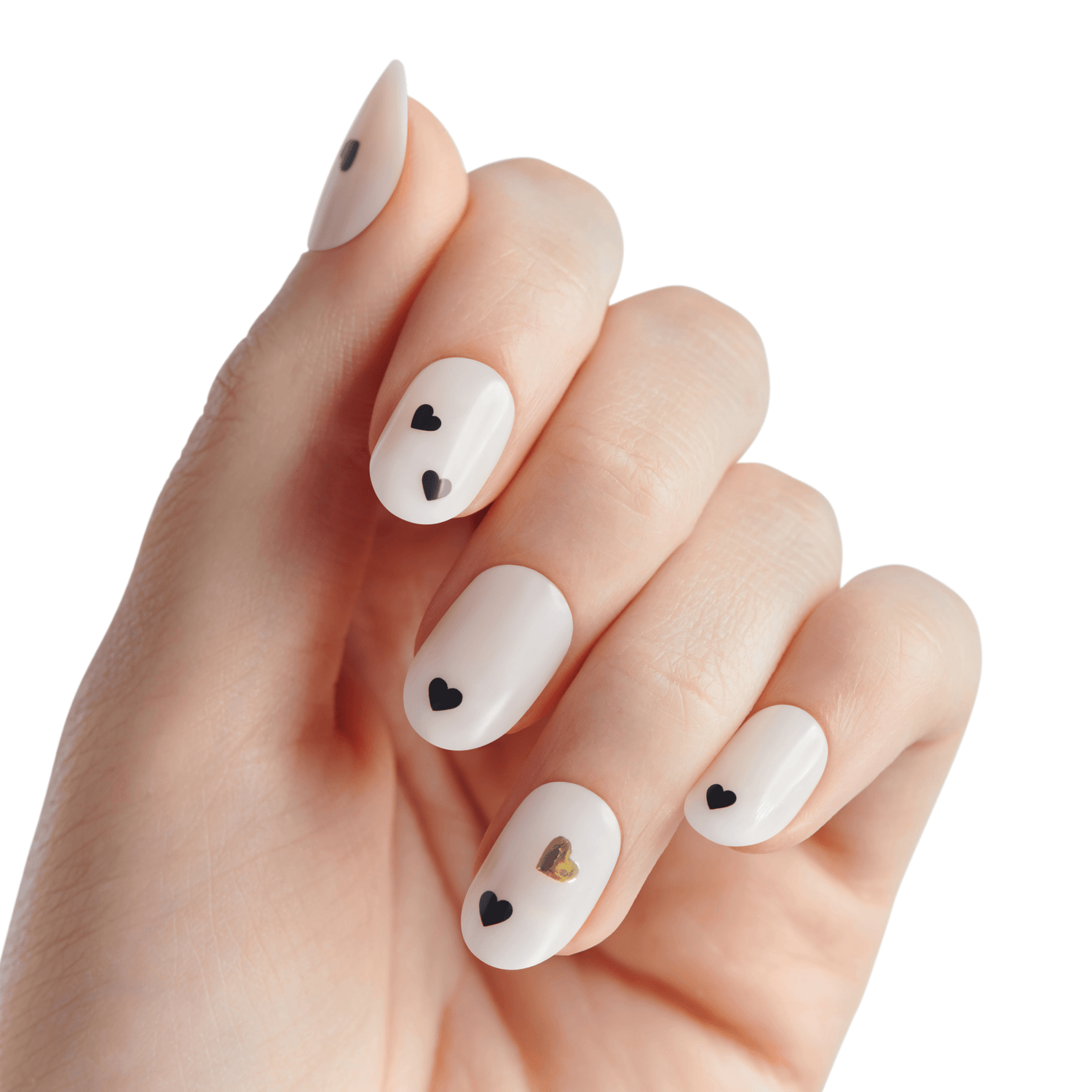 Hand with white press-on nails featuring small black heart designs on four nails and one gold heart on the ring finger, shown against a white background.