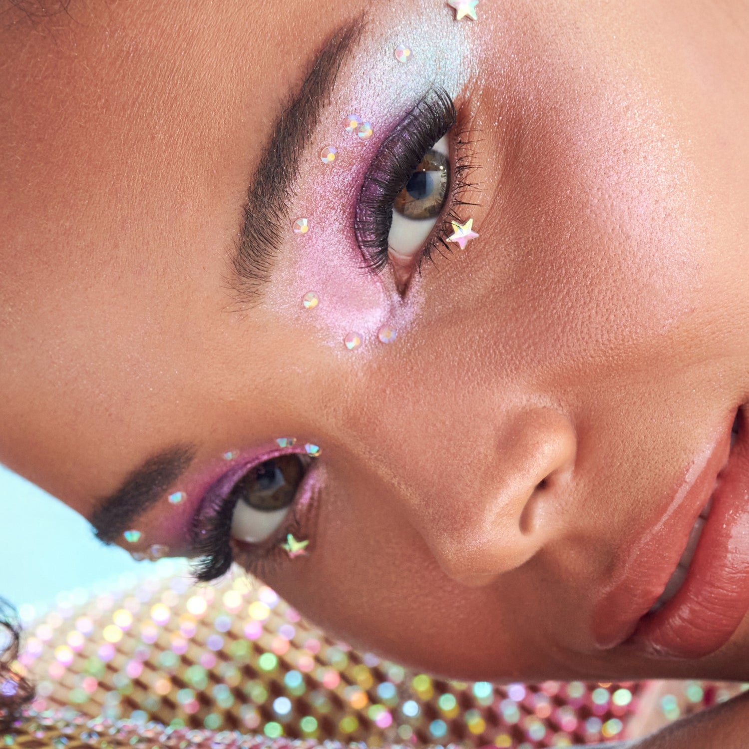 Artistic eye makeup with pink and purple eyeshadow, iridescent gems, and dramatic lashes.