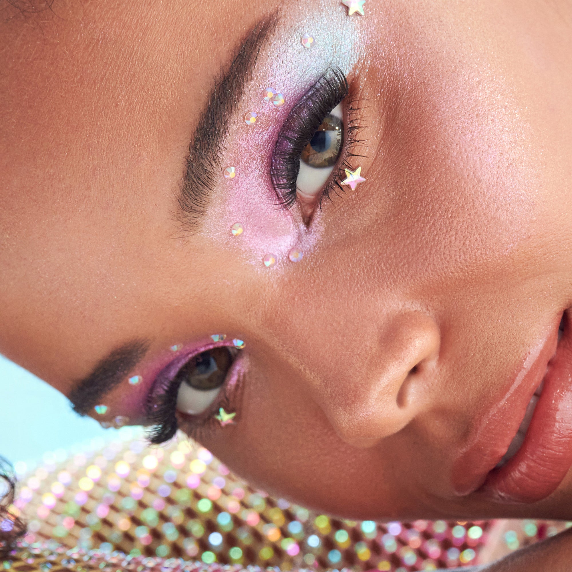 Artistic eye makeup with pink and purple eyeshadow, iridescent gems, and dramatic lashes.