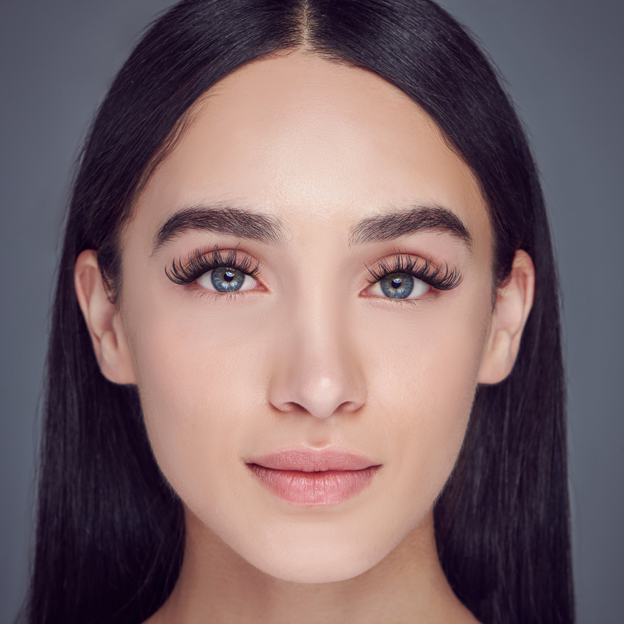 Close-up of a woman with straight dark hair wearing voluminous, curly false eyelashes that enhance her blue eyes and natural makeup look.