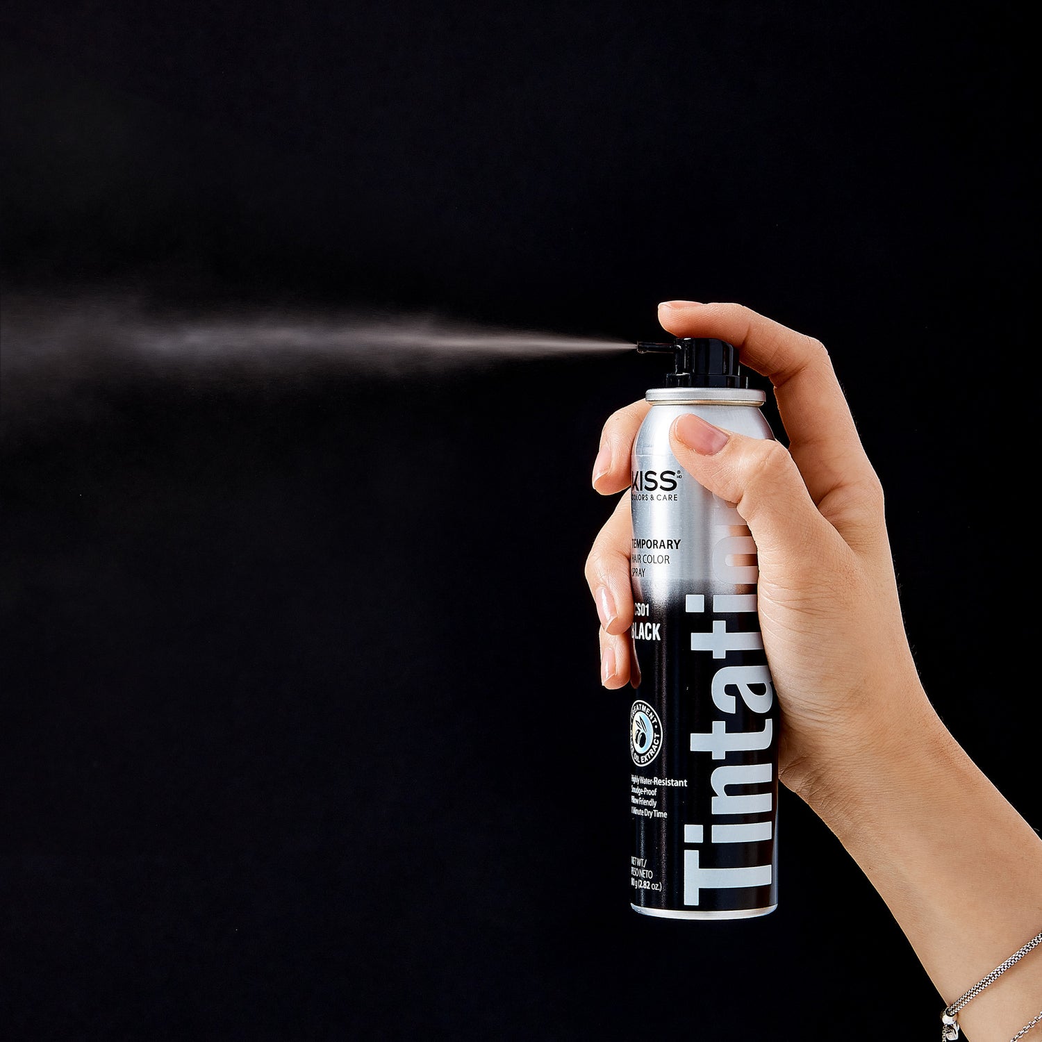 Hand holding and spraying a silver and black can of KISS Colors &amp; Care Tintation Spray in Natural Black, labeled as temporary, water-resistant, and smudge-proof.