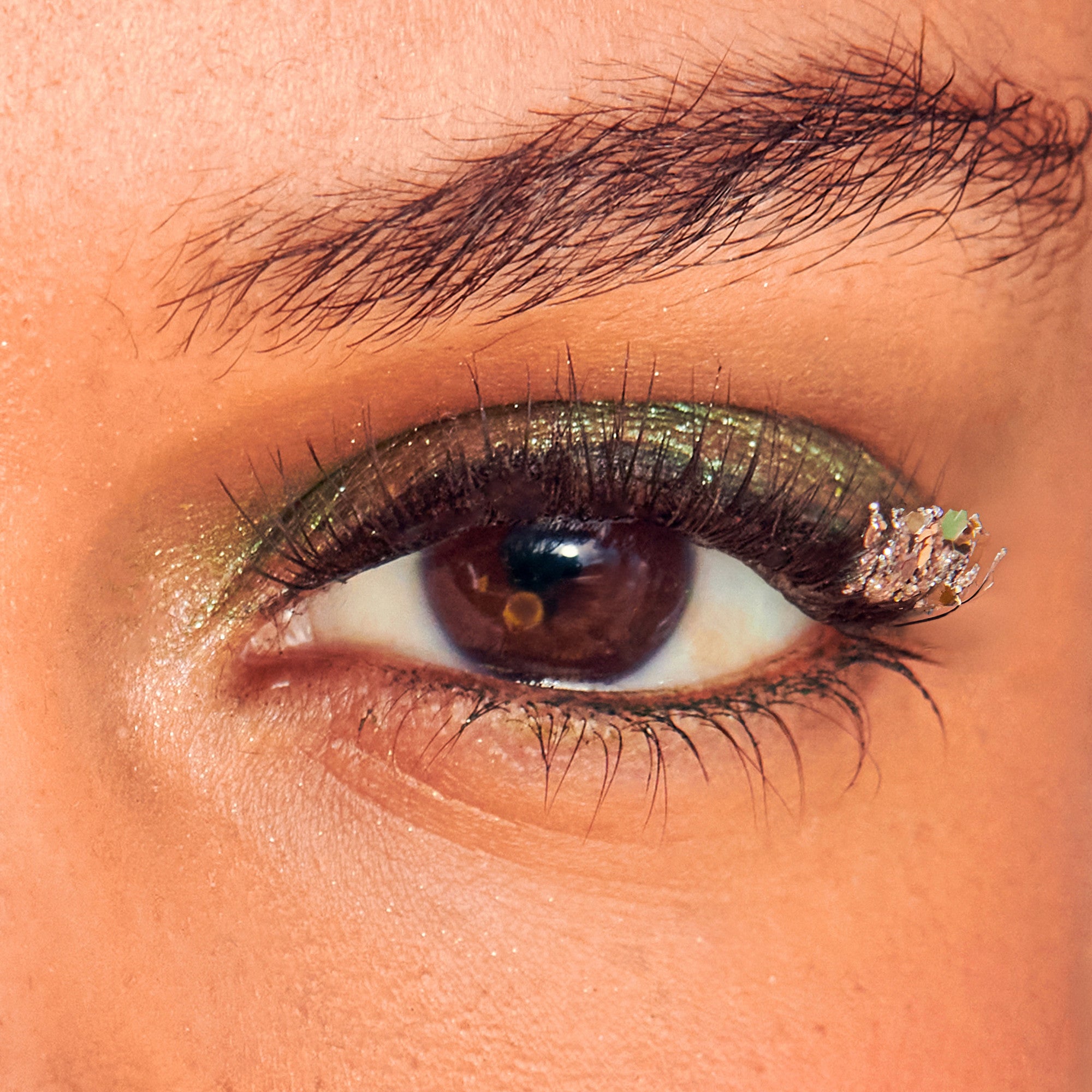 Close-up of eye with bronze glitter eyeshadow and black eyeliner on warm-toned skin.