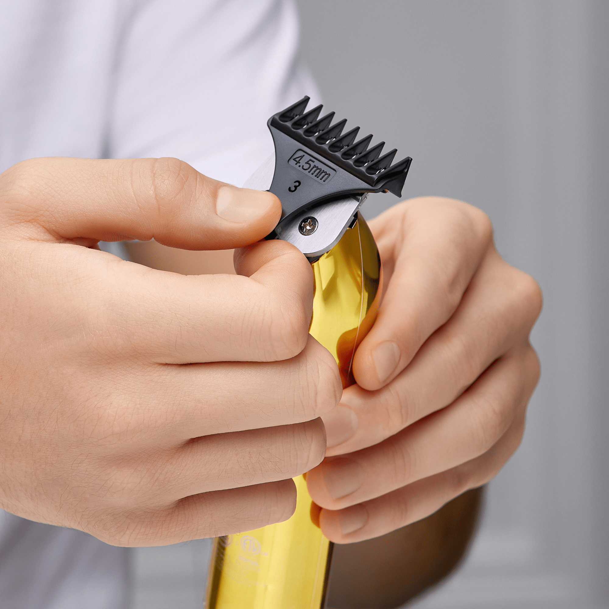 Hands holding a gold cordless T-blade beard and hair trimmer, attaching a black 4.5mm guide comb labeled \