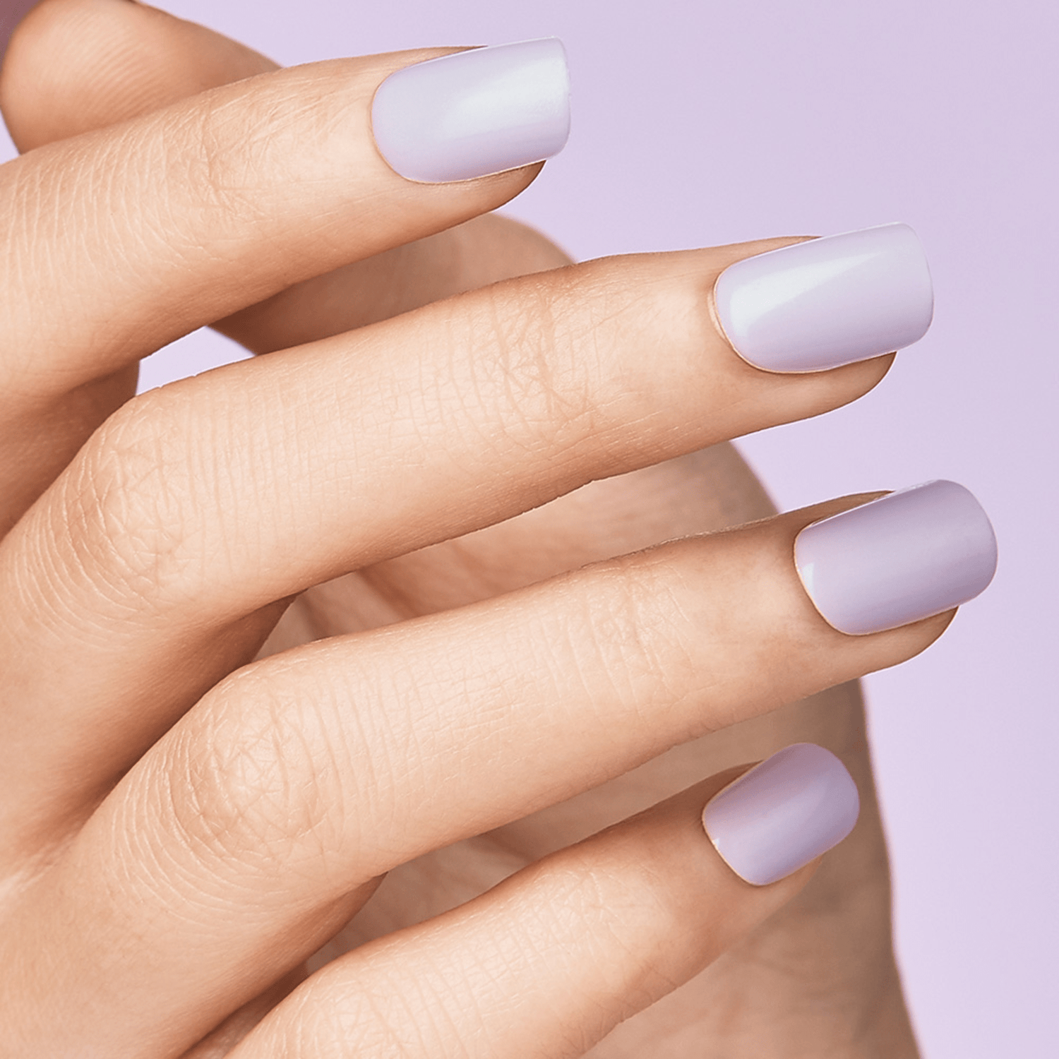 Hand with evenly shaped press-on nails in a soft pastel purple shade against a matching light purple background.