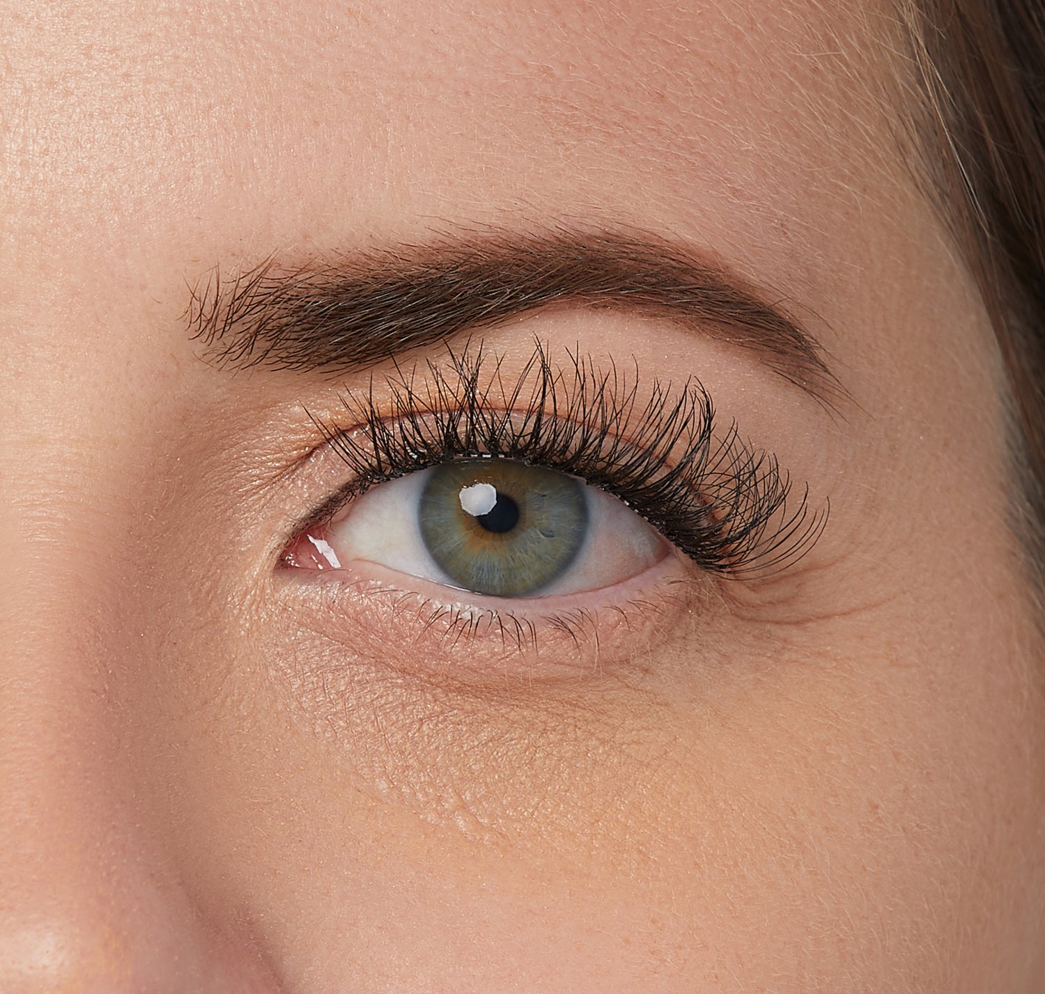 Close-up of a green eye with long, full, black self-adhesive false eyelashes applied, showcasing natural lash enhancement and curl.